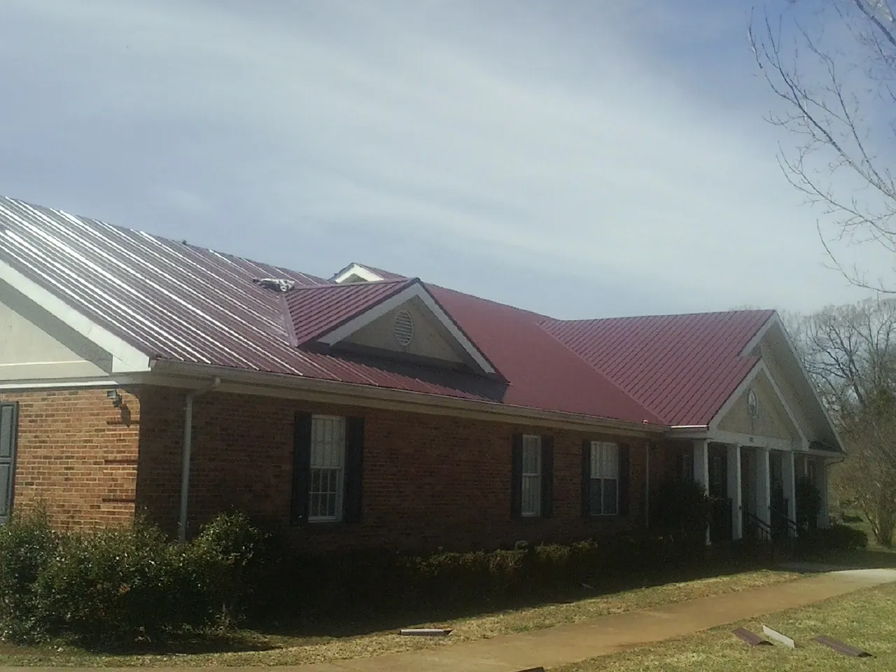 Red metal roof with gabled entries on a long brick building, from a Hail Damage Roof Repair job in Curlew