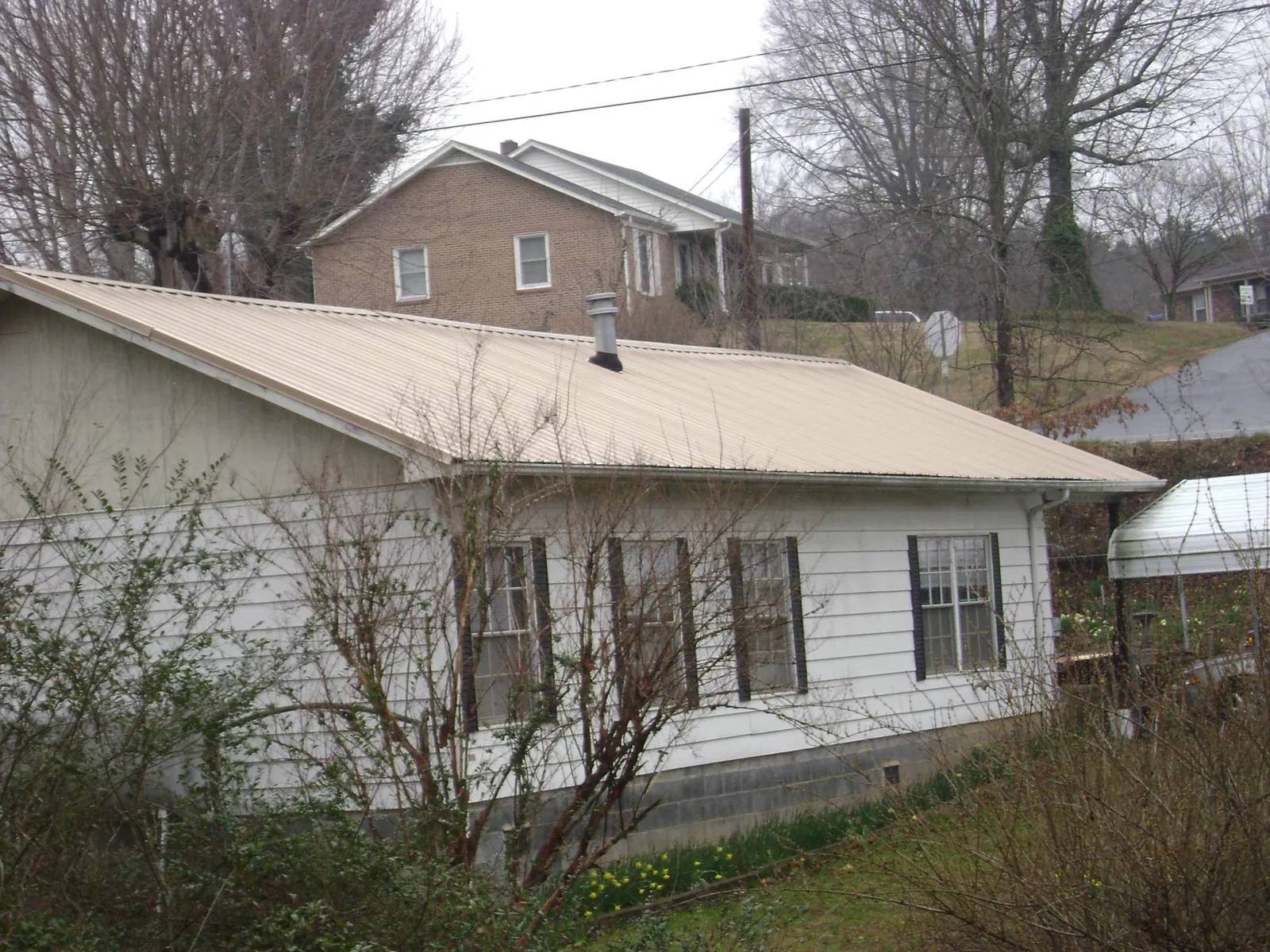 Tan metal roof on a white sided house set into a hillside — Commercial Roofing by Roofing Brothers in Curlew